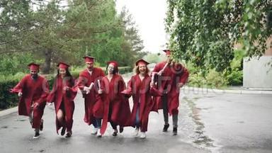 令人兴奋的<strong>毕业</strong>学生带着<strong>毕业证书</strong>在校园里奔跑，他们穿着长袍和传统的帽子，这是。